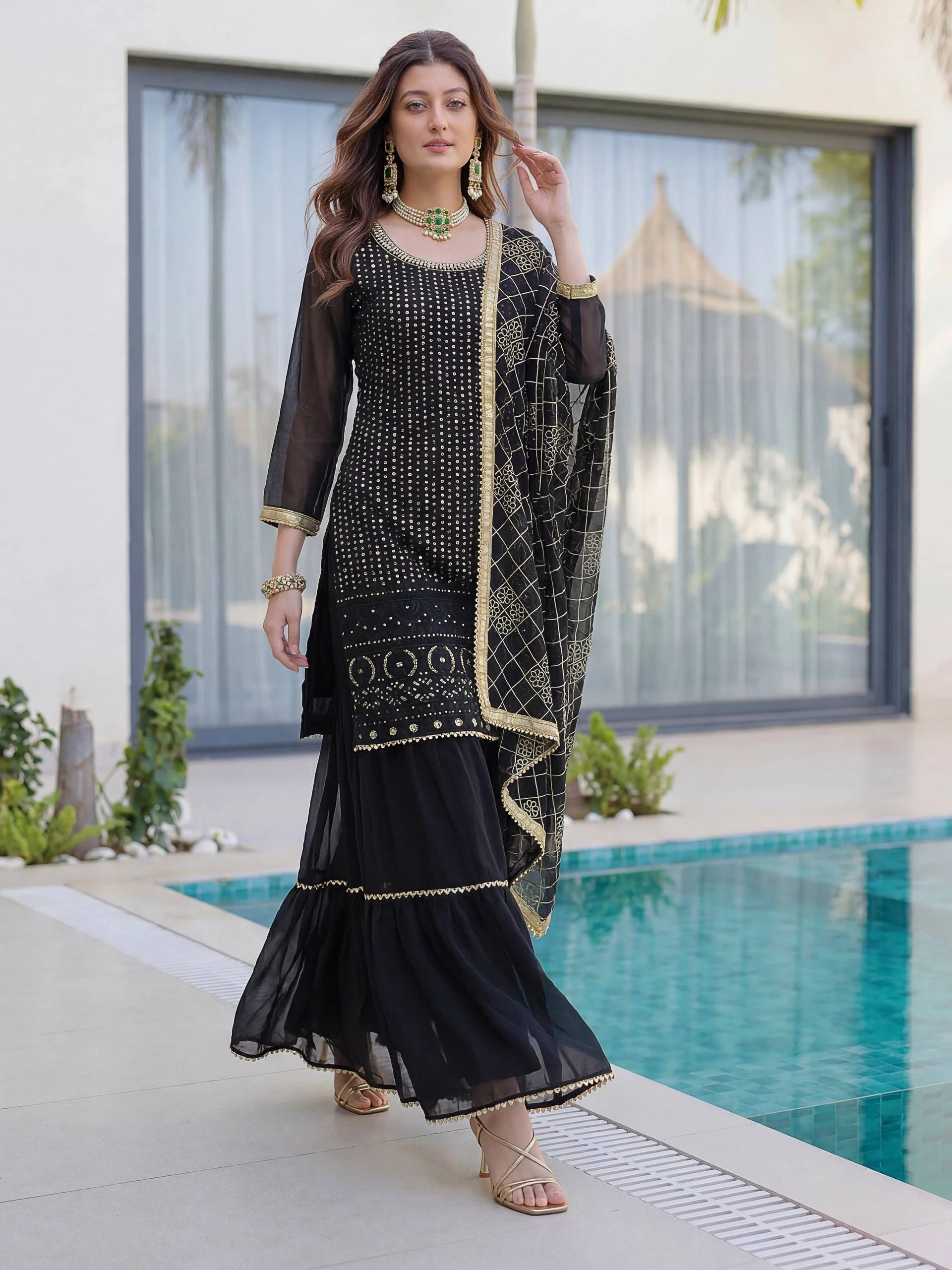 Woman in a black traditional outfit standing by a poolside.